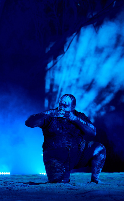 Two Noongar men perform a dance. They are wearing neon paint on their faces and the lighting is blue. It is nightime.